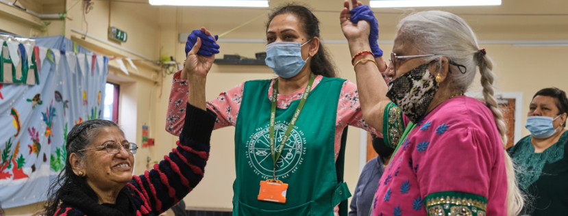 three indian women in a care home are celebrating, two are wearing masks
