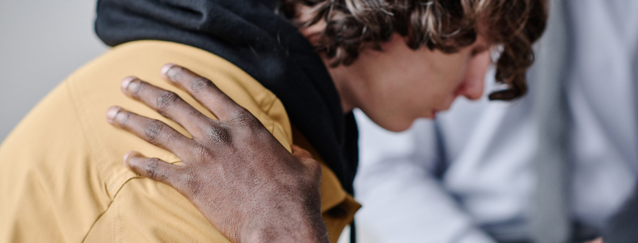 Lonely young adult with someone putting their hand on his shoulder