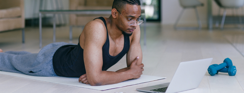 man lying down on yoga mat watching laptop