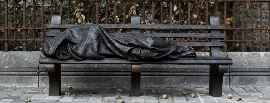 bronze statue of a homeless person on a bench